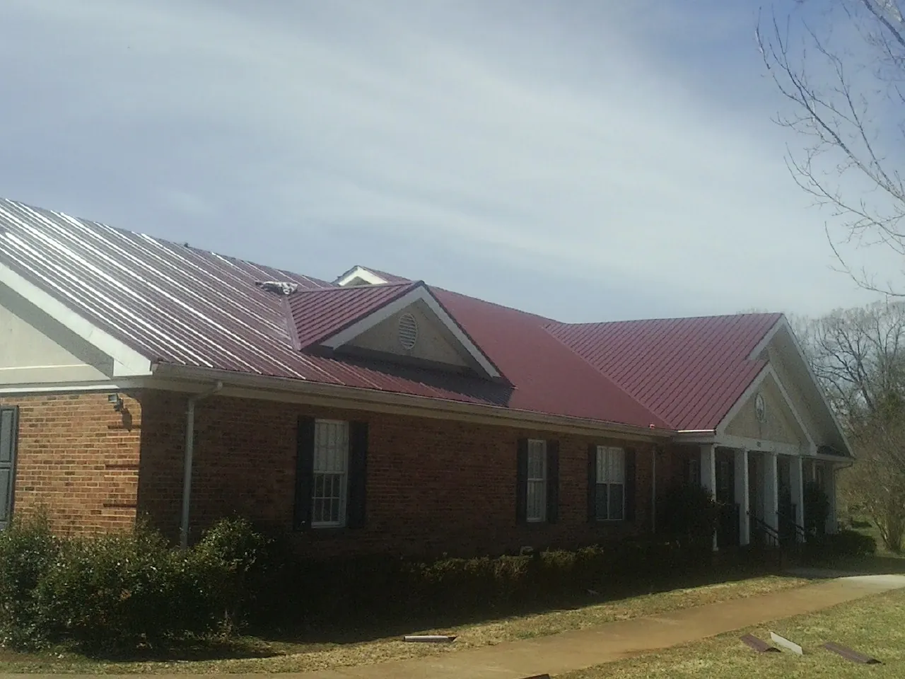 Red metal roof with gabled entries on a long brick building, from a Hail Damage Roof Repair job in Kennard