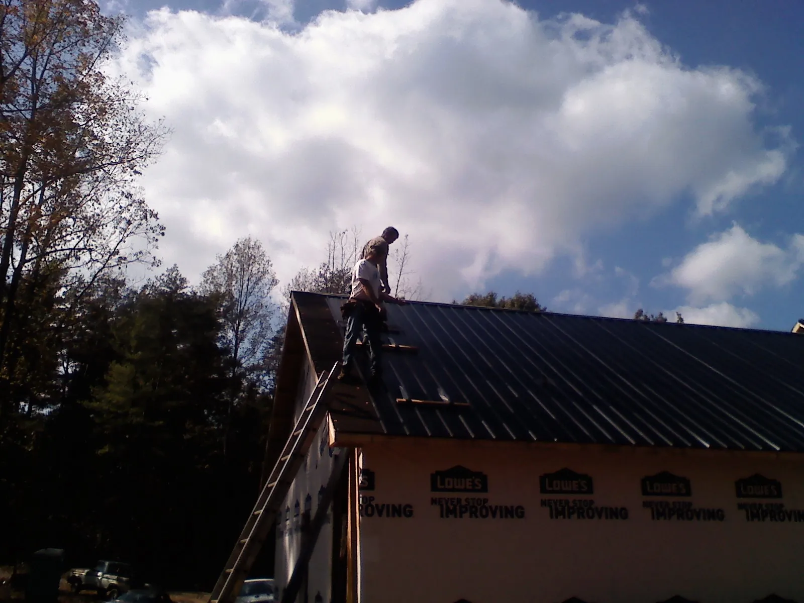 Roofer fastening dark metal panels high against a cloudy sky, from a Roof Inspection job in Kennard