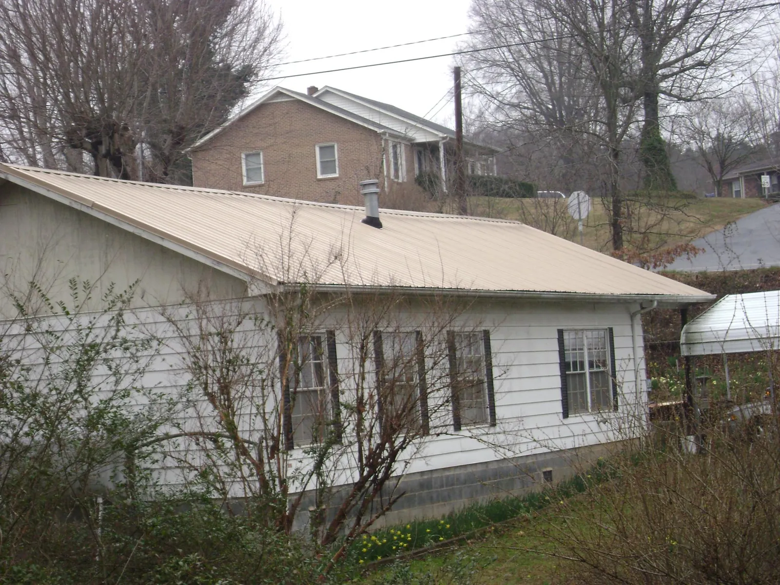 Tan metal roof on a white sided house set into a hillside — Commercial Roofing by Roofing Brothers in Kennard