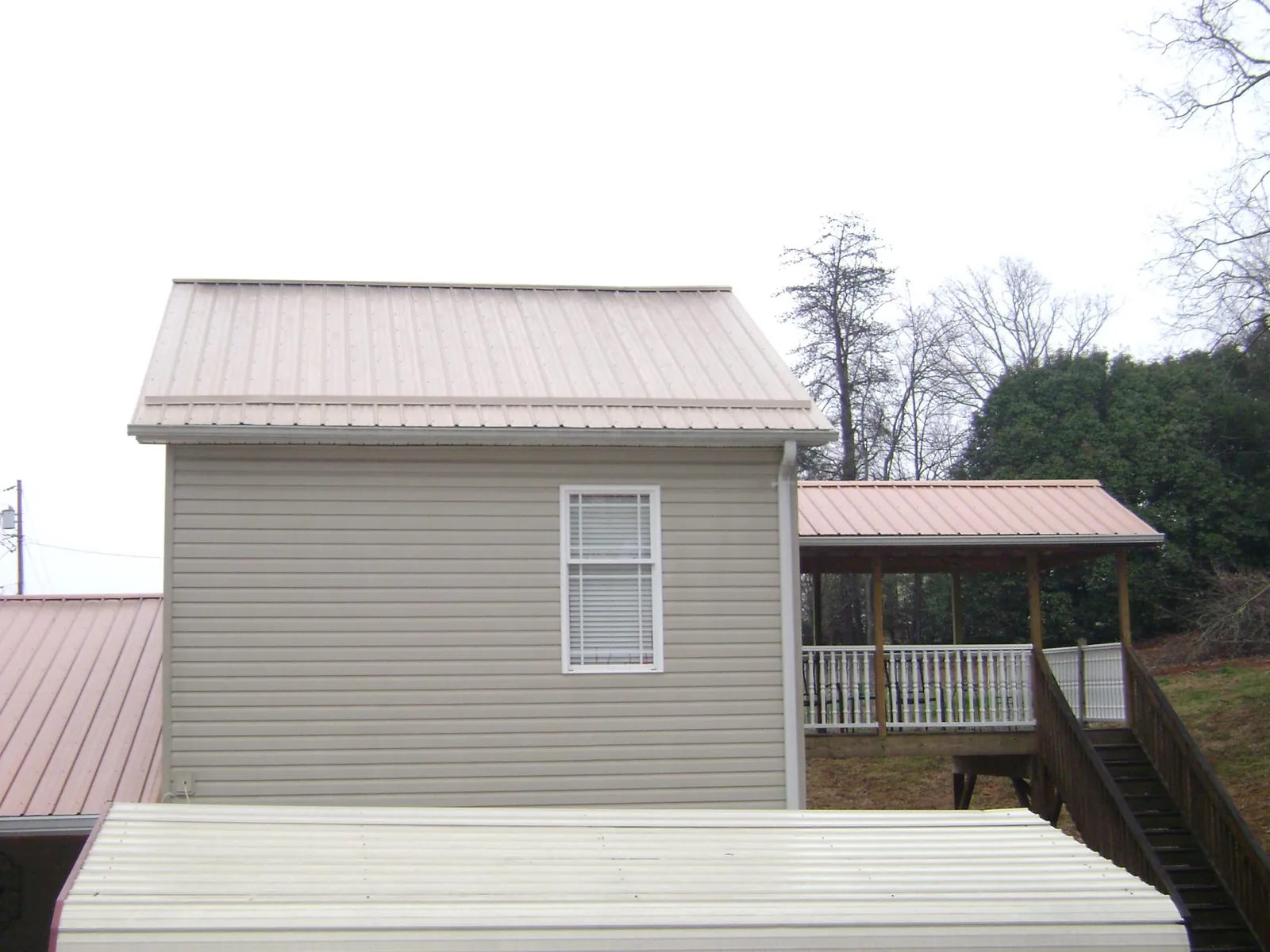 Tan metal roofs on a two story addition and attached porch, from a Roof Replacement job in Kennard